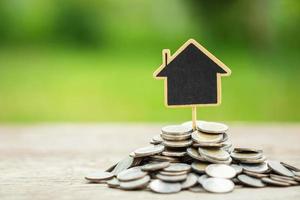 Wooden house model on the pile coin on wooden plank with nature space background. House investment concept photo