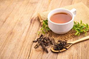 taza blanca de té caliente y hoja de té seca en la mesa de madera foto