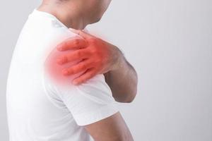 Close up man touching his shoulder and feeling a pain. Studio shot isolated on grey background with copy space for text photo