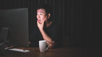 Early working in the morning concept, Asian man working on computer in the dark room and looking to screen with exciting face photo