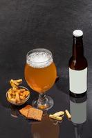 Glasses with different types of craft beer on a wooden bar. In glasses and bottles. Nuts and crackers on the table. On a dark background. photo