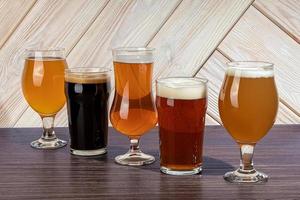 Glasses with different types of craft beer on a wooden bar. In glasses and bottles. Nuts and crackers on the table. On a dark background. photo