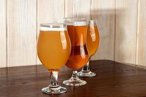 vasos con diferentes tipos de cerveza artesanal en una barra de madera. en vasos y botellas. nueces y galletas en la mesa. sobre un fondo oscuro. foto