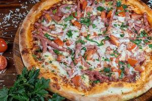 Pizza with bacon and cheese, herbs and cherry tomatoes. With mozzarella, shrimps and octopuses, mussels and other products on a wooden background. photo