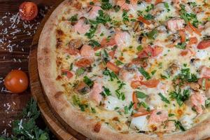 Pizza with bacon and cheese, herbs and cherry tomatoes. With mozzarella, shrimps and octopuses, mussels and other products on a wooden background. photo