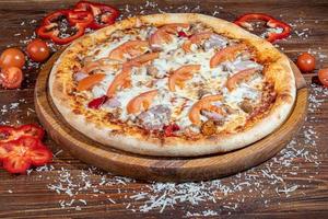 Pizza with bacon and cheese, herbs and cherry tomatoes. With mozzarella, shrimps and octopuses, mussels and other products on a wooden background. photo