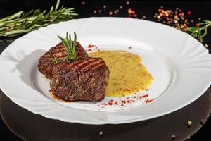 Meat dish on a plate with sauce. Chicken breast, fried pork. Parsley. Mustard sauces and ketchup. On a dark background. photo