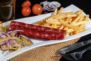 Smoked sausages with french fries and pickles. Snack for beer. Dark background. photo