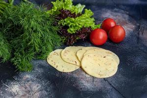 Sliced cheese with slices of tomatoes and bell peppers. Along with spring vegetables. On a dark background. photo