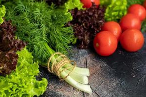 Fresh vegetables for salad. Tomatoes and lettuce, cucumbers with zucchini and cabbage with dill. Spring harvest, benefits and vitamins. On a dark background. photo