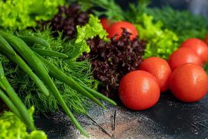 Fresh vegetables for salad. Tomatoes and lettuce, cucumbers with zucchini and cabbage with dill. Spring harvest, benefits and vitamins. On a dark background. photo