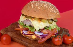 Delicious burger on the board with cutlet, tomatoes and cheese, cucumber and lettuce. On a red background. Fast food. photo