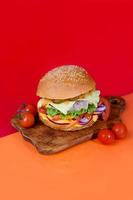 Delicious burger on the board with cutlet, tomatoes and cheese, cucumber and lettuce. On a red background. Fast food. photo