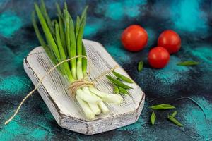 cebollas verdes para ensalada o fritata. cosecha de primavera, beneficios y vitaminas. sobre un fondo oscuro. foto