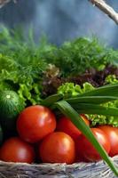 Fresh vegetables for salad in a basket. Tomatoes and cucumbers with zucchini and cabbage with dill. Spring harvest, benefits and vitamins. On a dark background. photo