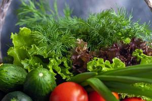 Fresh vegetables for salad. Tomatoes and lettuce, cucumbers with zucchini and cabbage with dill. Spring harvest, benefits and vitamins. On a dark background. photo