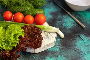 Fresh vegetables for salad. Tomatoes and lettuce, cucumbers with zucchini and cabbage with dill. Spring harvest, benefits and vitamins. On a dark background. photo