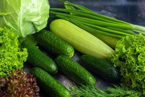 Fresh vegetables for salad. Tomatoes and lettuce, cucumbers with zucchini and cabbage with dill. Spring harvest, benefits and vitamins. On a dark background. photo