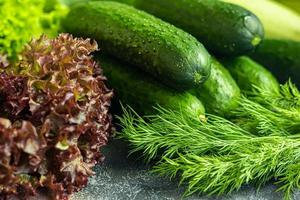 Fresh vegetables for salad. Tomatoes and lettuce, cucumbers with zucchini and cabbage with dill. Spring harvest, benefits and vitamins. On a dark background. photo