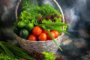 verduras frescas para ensalada en una cesta. tomates y pepinos con calabacín y repollo con eneldo. cosecha de primavera, beneficios y vitaminas. sobre un fondo oscuro. foto