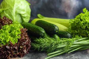Fresh vegetables for salad. Tomatoes and lettuce, cucumbers with zucchini and cabbage with dill. Spring harvest, benefits and vitamins. On a dark background. photo