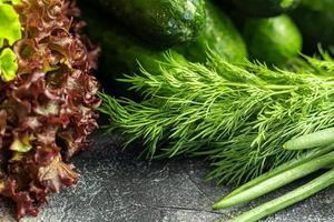 Fresh vegetables for salad. Tomatoes and lettuce, cucumbers with zucchini and cabbage with dill. Spring harvest, benefits and vitamins. On a dark background. photo