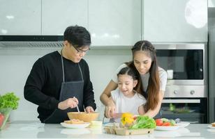 familia asiática que están cocinando juntos felizmente en la cocina de la casa. foto