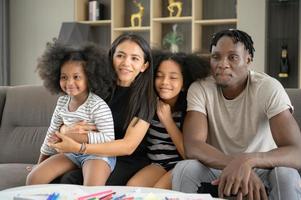 familia asiático-afroamericana relajándose, charlando, pintando y divirtiéndose de vacaciones en la sala de estar de la casa foto