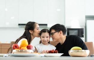 el padre y la madre asiáticos muestran su amor a la pequeña hija y desayunan juntos felizmente en el comedor de la casa. foto