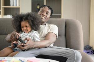 padre e hijo asiático-afroamericanos se relajan jugando juegos de computadora en la sala de estar de la casa. foto