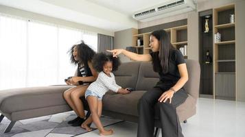 Asian-African American family relaxing, chatting, painting and having fun on vacation in the living room of the house photo