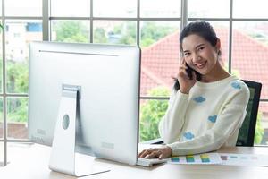 Work from home and online learning concept. Pretty young women working on computer look at the screen using smartphone in the living room or co-working space. Student study online training course. photo