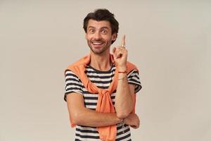 Happy handsome young man with stubble in striped t shirt and sweater on shoulders pointing up using forefinger and having an idea over white background photo