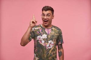 Young attractive wondered man wearing flowered t-shirt and glasses, looking at camera with happy expression, showing thumb up, isolated over pink background photo