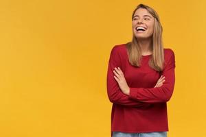 Laughing happy girl, turned to the left side, stands with folded arms isolated on a yellow background. Funny joke, pleasant moment, free space for your advertisement