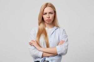 Unhappy attractive blonde female standing over white background with crossed arms, looking sad and going to cry, wearing casual clothes photo