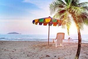 White beach chair and umbrella on tropical beach with orange sky photo