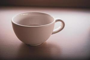 una vieja taza de té blanca se colocó sobre la mesa por la mañana con luz y sombra. foto