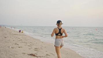 mulher correndo na praia do oceano. jovem mulher asiática se exercitando ao ar livre correndo à beira-mar. conceito de corrida saudável e exercício ao ar livre. atleta ativo e esportivo correndo. verão ativo video