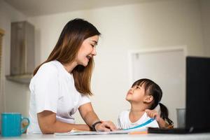 feliz madre e hija sonriente juntas pintando con marcadores. madre ayudando a su hijo adoptado con la tarea de arte. madre alegre y niña asiática haciendo pintura en casa. foto