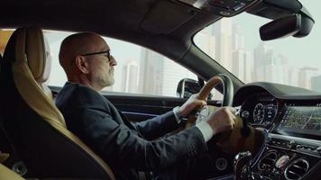 een bentley-chauffeur in een pak past de achteruitkijkspiegel aan.achtergrond,stad,gebouwen,wolkenkrabbers video