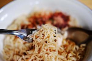 Tradición comida tailandesa fideos instantáneos de mariscos calientes y picantes en un tazón blanco con tenedor y cuchara sobre fondo de piso de madera foto