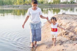 A young mother plays with her 2-5 year old daughter on the beach in summer. Outdoor resort on the lake Have a good rest on weekends, family days. photo