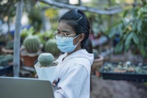 Hermosa trabajadora de invernadero asiática que vende pequeñas plantas en las redes sociales en vivo con el móvil. Paisajismo de árboles pequeños y decoración del jardín del hogar jardinero. foto