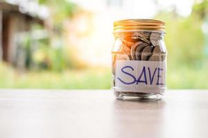 Coins and text SAVE in a glass jar placed on a wooden table. Concept of saving money for investment and emergency situations. Close up, Blurred background photo