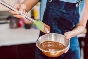 mujer mezclando suave y delicioso ganache de chocolate oscuro con batidor en un tazón de plata. foto