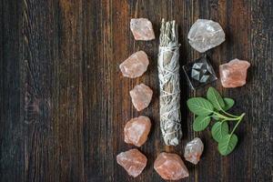 group of healing objects of smudge sage stick, pink salt crystals, and fresh sage with copy space flat lay photo