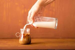 la mano está vertiendo leche en café preparado en estudio con espacio para copiar. foto