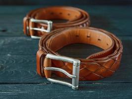 two leather brown belts on dark wooden background photo