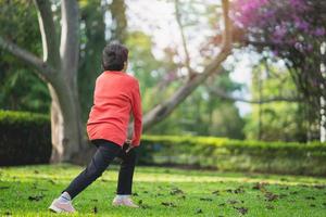 Senior asian woman body warming before exercising. Old woman stretching before jogging in garden, Sport athlete running concept. photo